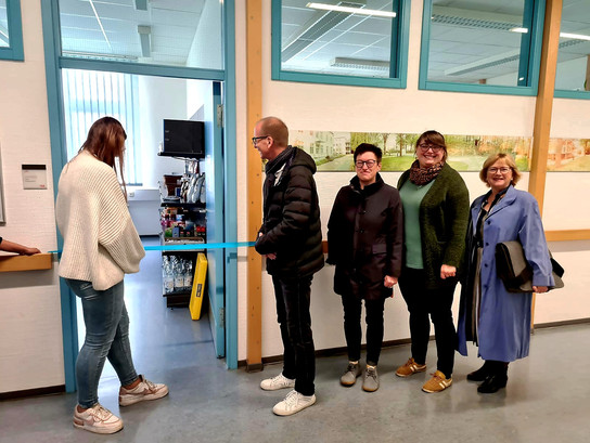 Mitarbeiterinnen und Mitarbeiter des SRH Berufsbildungswerkes Dresden stehen am neu eröffneten Kiosk. Eine Auszubildende schneidet zur Eröffnung ein blaues Band durch. 